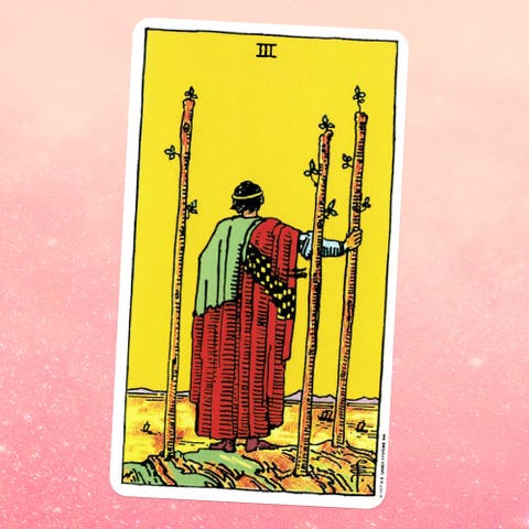 the tarot card the three of wands, showing a person in robes holding a wooden staff and looking off into the distance, with two more staffs next to them