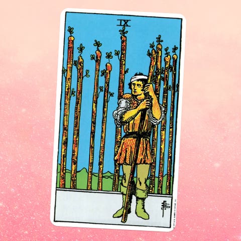 the tarot card the nine of wands, showing a person in aa tunic holding a wooden staff with eight more behind them